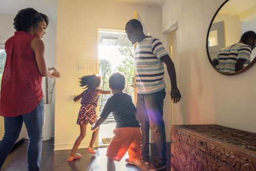 Divorced parents are standing in the hall as their children are running towards an open front door in excitement Visual concept for legal blog discussing 50/50 child custody in Utah.
