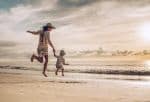 mother and son holding hands while jumping on the beach at sunset. - Ashley Wood Law, P.C.