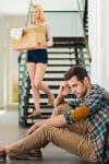Frustrated young man sitting on the floor of his apartment while his girlfriend is leaving with boxes - Ashley Wood Law, P.C.