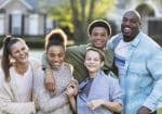 A multi-ethnic blended family of five standing together outdoors in their front yard, smiling and laughing, looking at the camera. The African-American father is in his 40s. Their son and daughter from his prior marriage are 13 year old twins, mixed race African-American and Caucasian. The mother is in her 30s and their youngest son from her prior marriage is 11 years old.