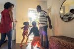 Divorced parents are standing in the hall as their children are running towards an open front door in excitement Visual concept for legal blog discussing 50/50 child custody in Utah.